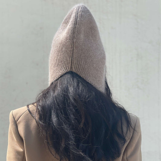 Person wearing a dark beige knitted beanie and coat against a plain background.