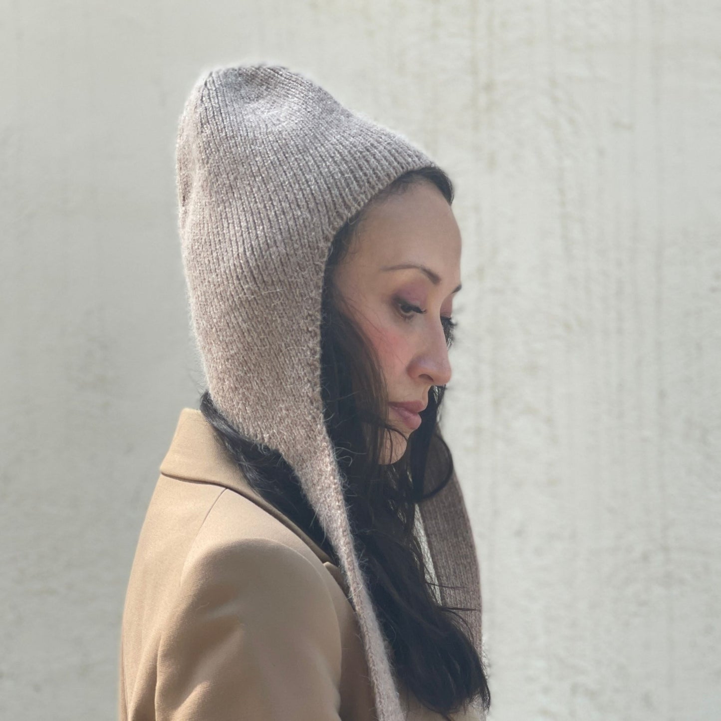 Woman wearing a beige coat and knitted bonnet against a light gray background.