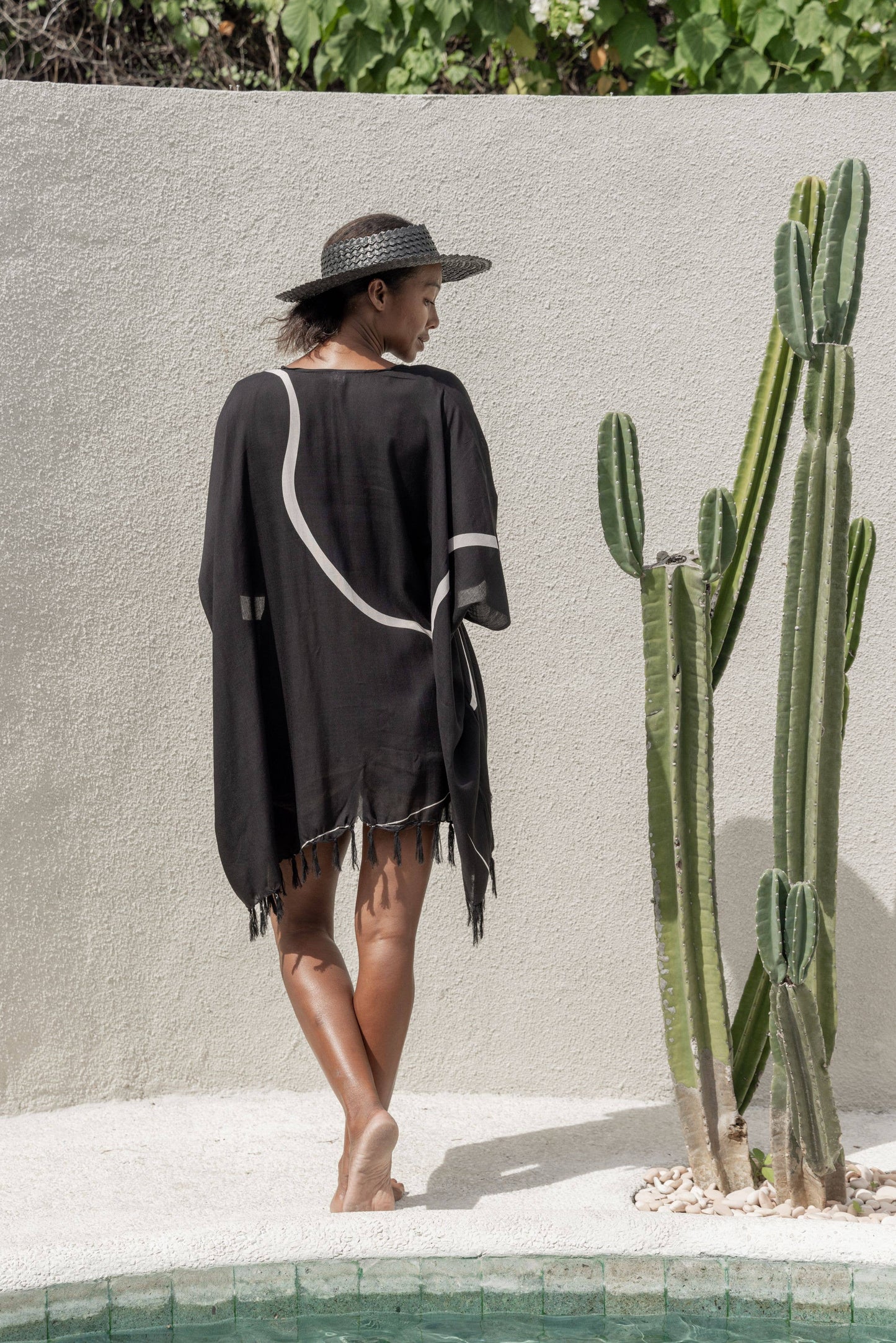 Back view of Papale Sun Hat in Black. Model wears with black kimono by the pool.