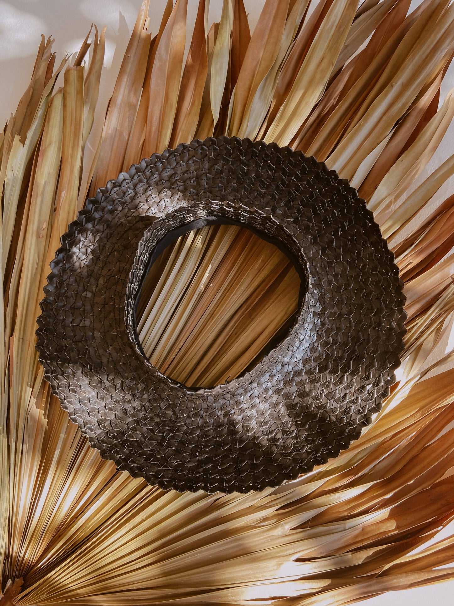 Birdseye view of Papale Sun Hat in Black. Hat sits on large leaves, outside in sunshine.