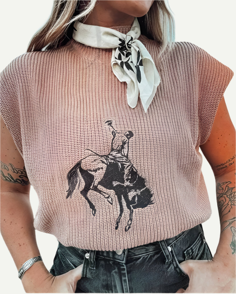 Blush knit short-sleeve sweater with embroidered bronc rider motif, styled with black jeans and white neck scarf.