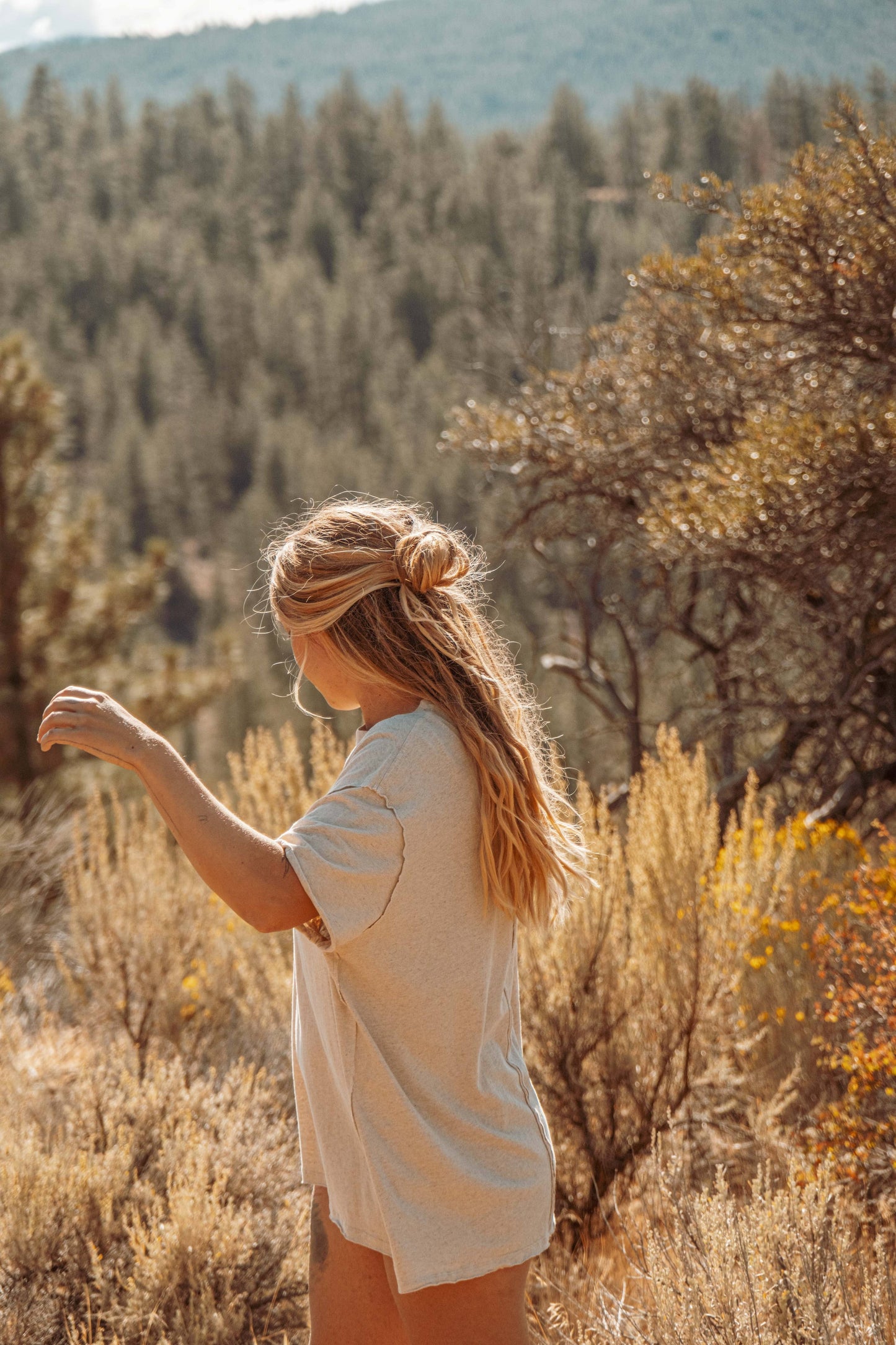 Lifestyle image of Hemp Organic Cotton Unisex T-Shirt. Model wears outside on sunny day with forest in background.
