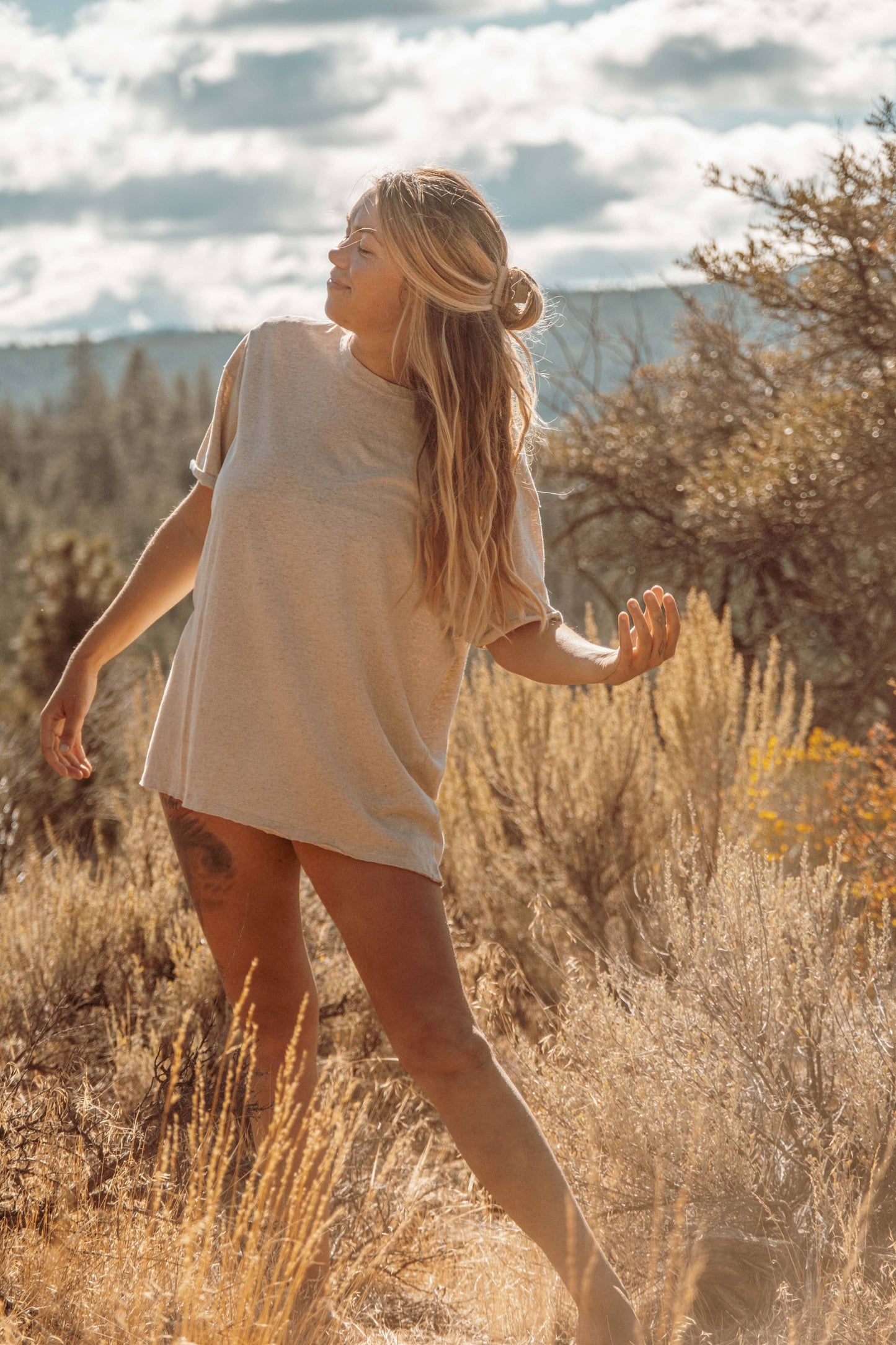 Lifestyle image of Hemp Organic Cotton Unisex T-Shirt. Model wears the t-shirt whilst sweeping hair to side.