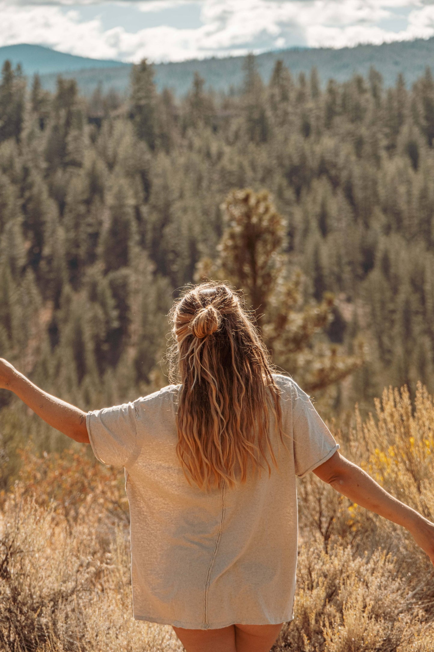 Lifestyle image of Hemp Organic Cotton Unisex T-Shirt. Model outside in nature on sunny day with forest in far background.