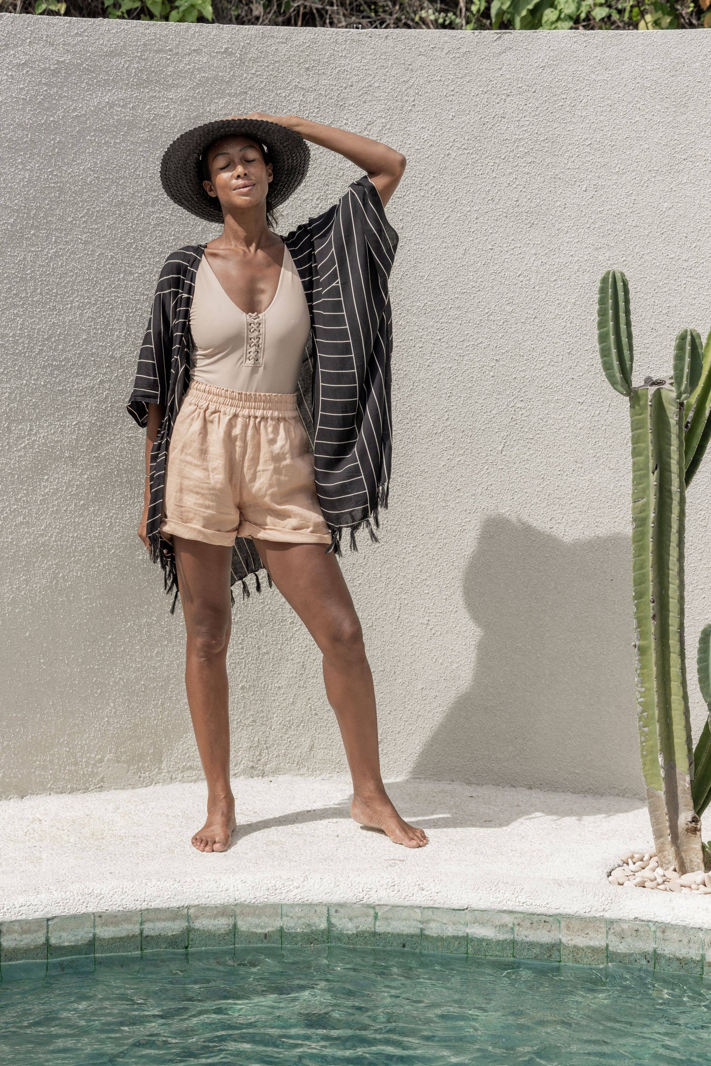 Lifestyle photo of model wearing Papale Sun Hat in Black by the pool and closing her eyes while enjoying the sun.