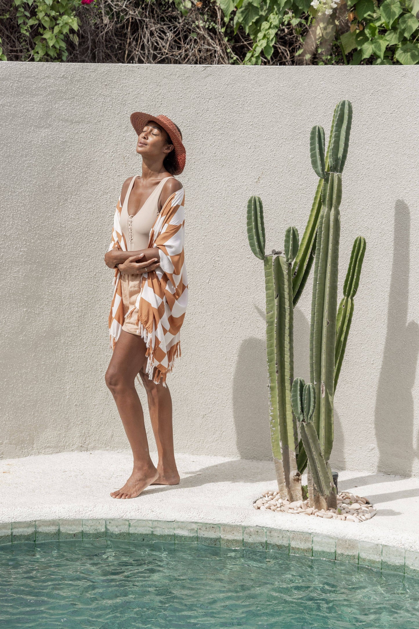 Lifestyle image of model wearing Papale Sun Hat in Clay standing by the pool and wearing a kimono.