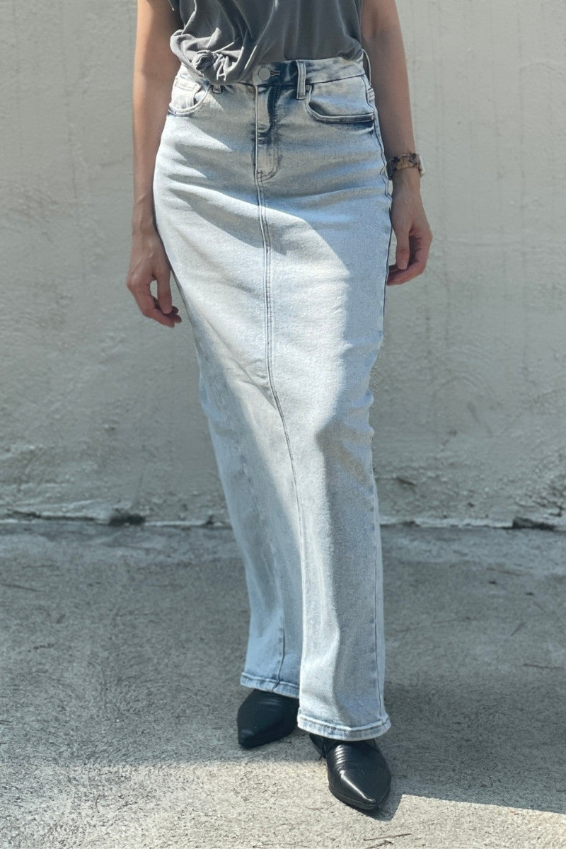 Model wearing light blue denim maxi skirt, black tee-shirt and black shoes against a plain background.