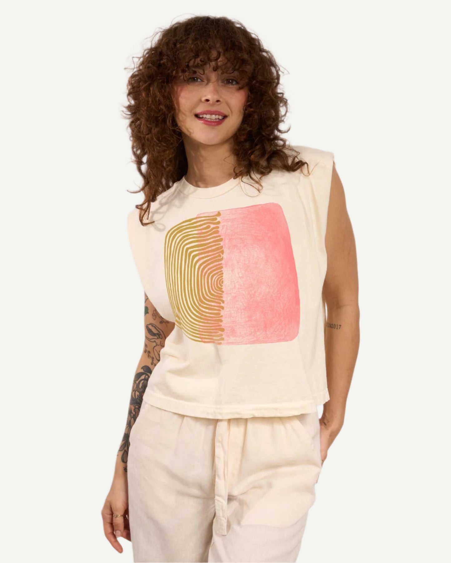 White Two Parts Muscle Tee with green and pink graphic by Go To Devil, styled on curly haired model with white pants.