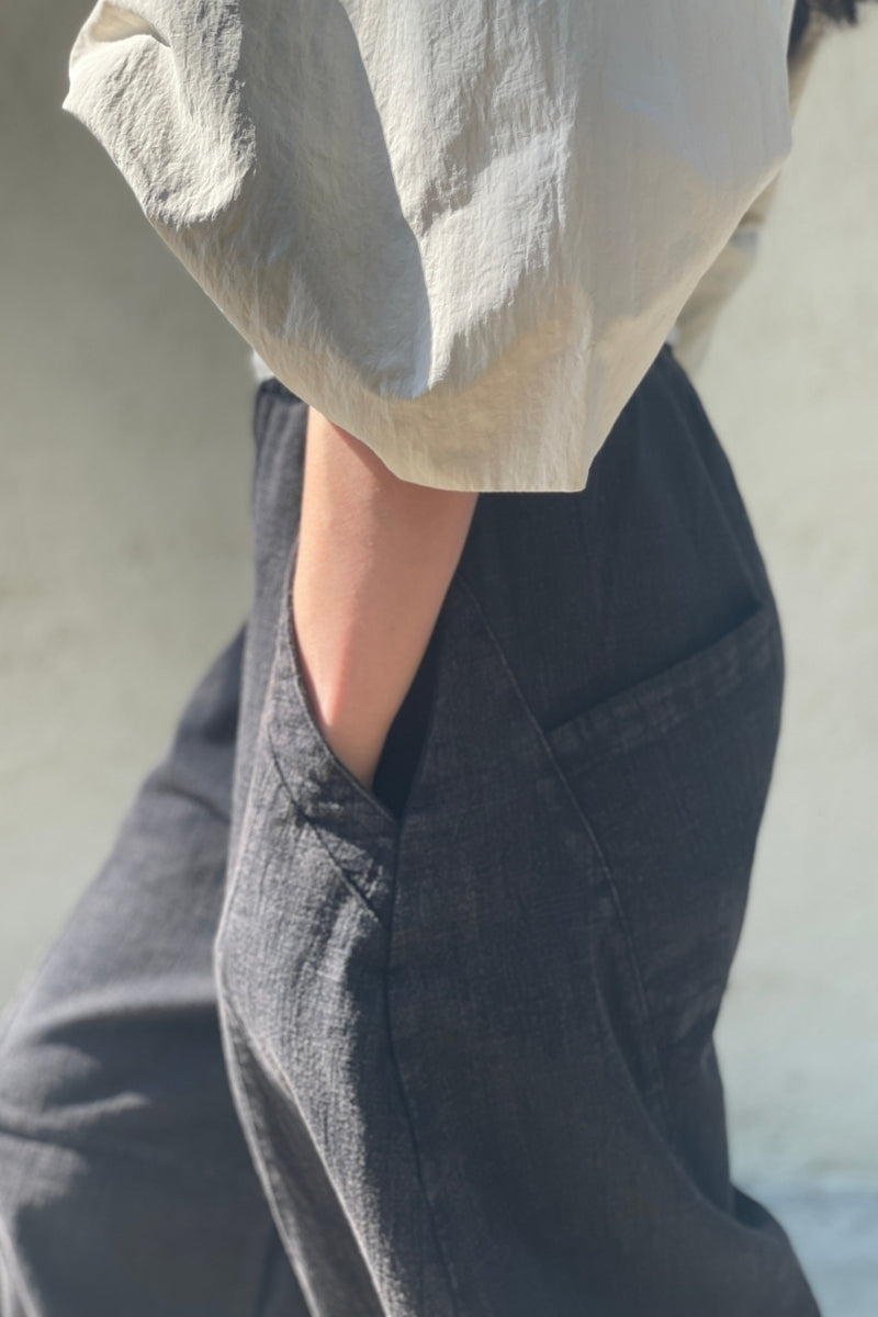 Person wearing a beige blouse with balloon sleeves and dark pants against a neutral background. Hands in pocket.