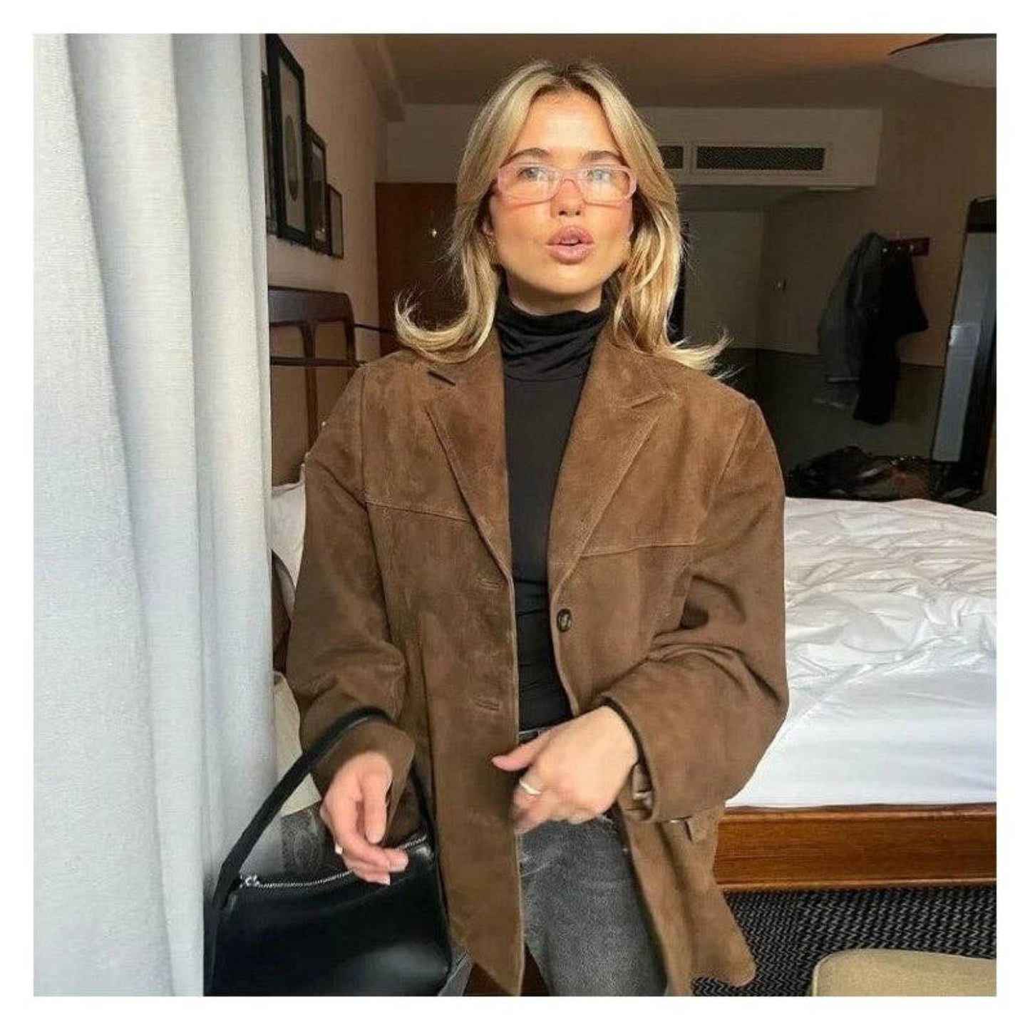 Brown cropped suede jacket with a minimal silhouette and vintage-inspired look. Model wears with glasses and black leather bag.