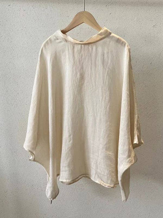 Cream linen blouse with airy batwing sleeves and lace-up back detail, shown  hanging in natural light.