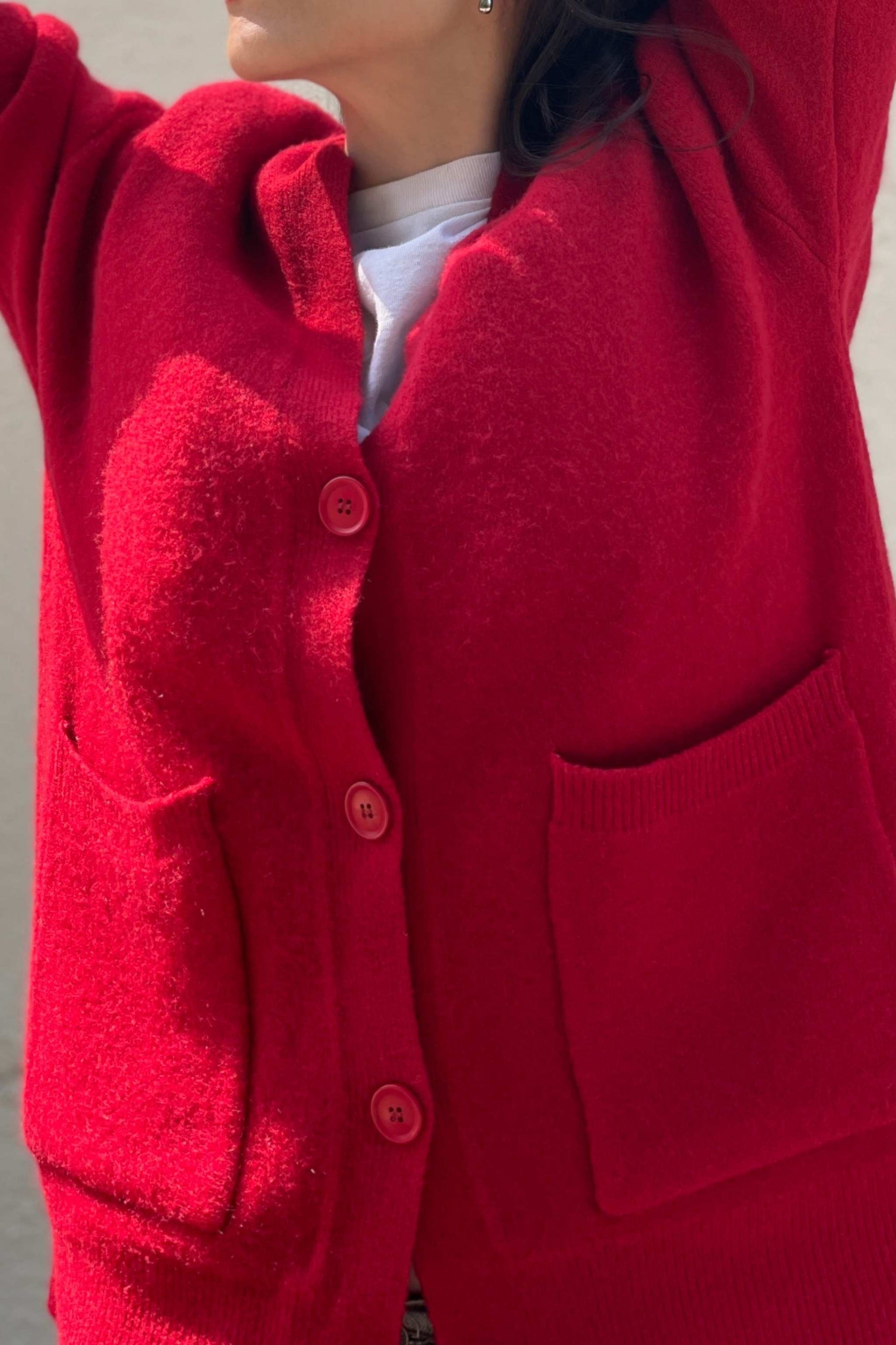 Close-up of oversized red cardigan with deep V-neck, showing soft knit texture and buttons, worn with white tee. 