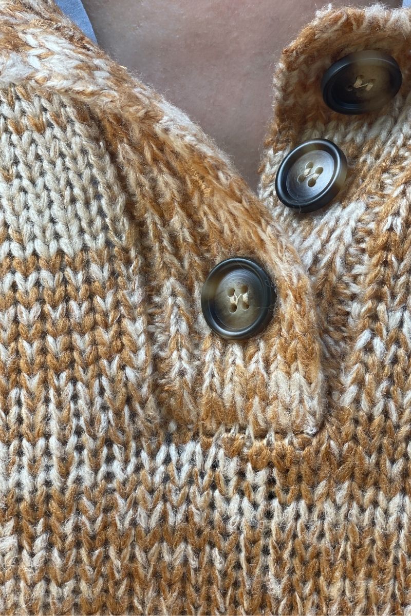 Close-up of a orange and beige knitted sweater with buttons.