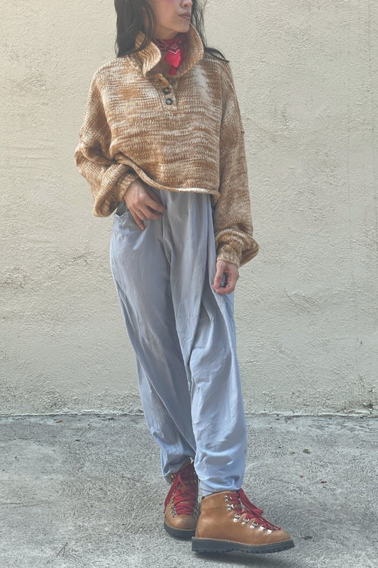Woman wearing a rust colored sweater, with collar over a light blue dress, with orange hiking boots, and red laces, standing against a plain wall.