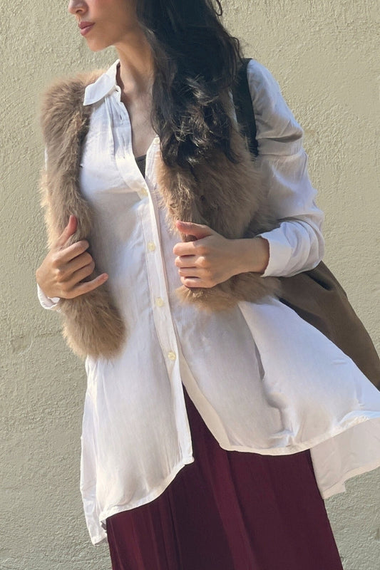 Woman wearing a white shirt and maroon skirt with a faux-fur vest against a beige wall.