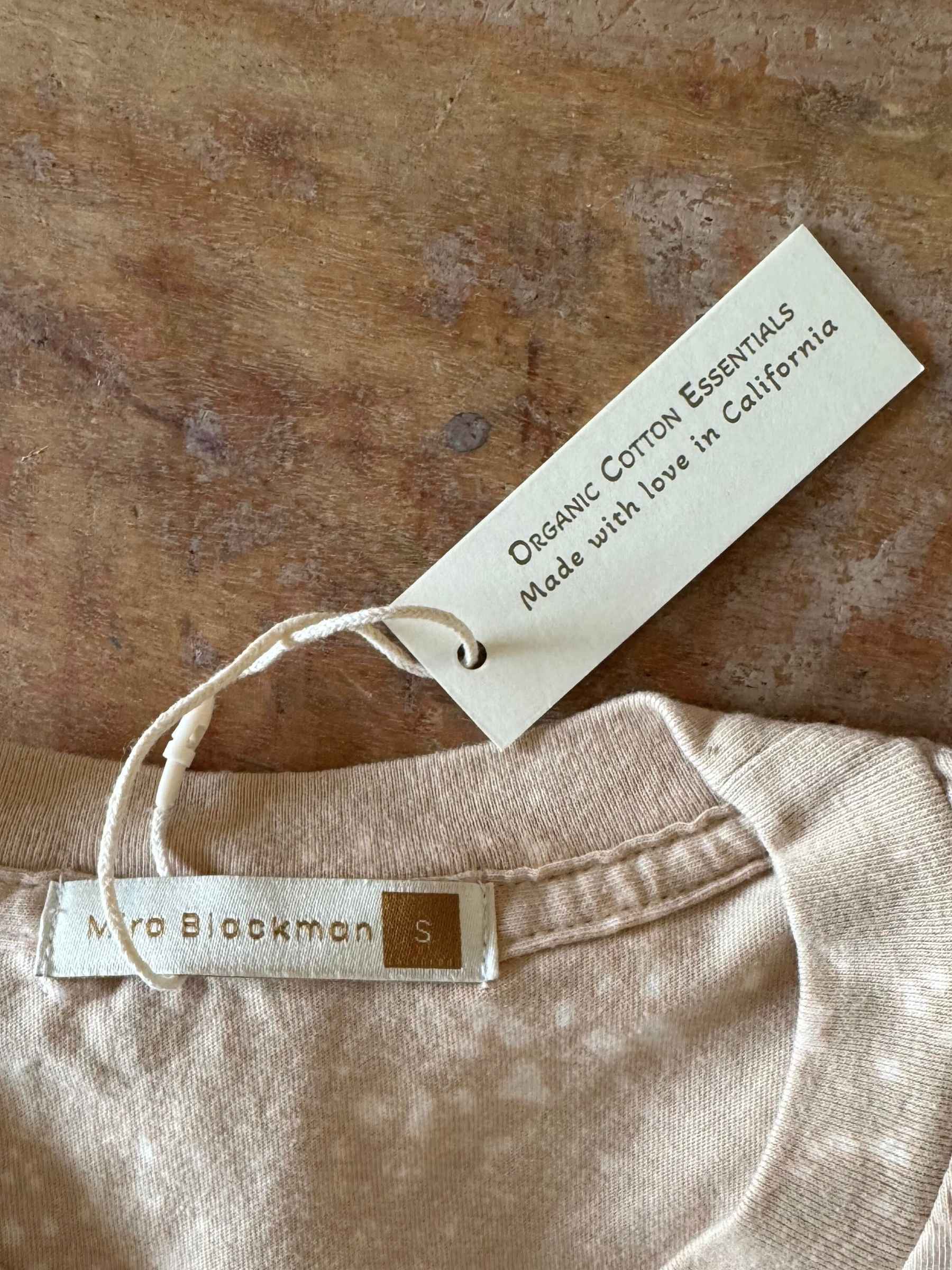Flay lay of Luminary Organic Tee by Mira Blackman in Neutral showing organic cotton and made with love in California label. 