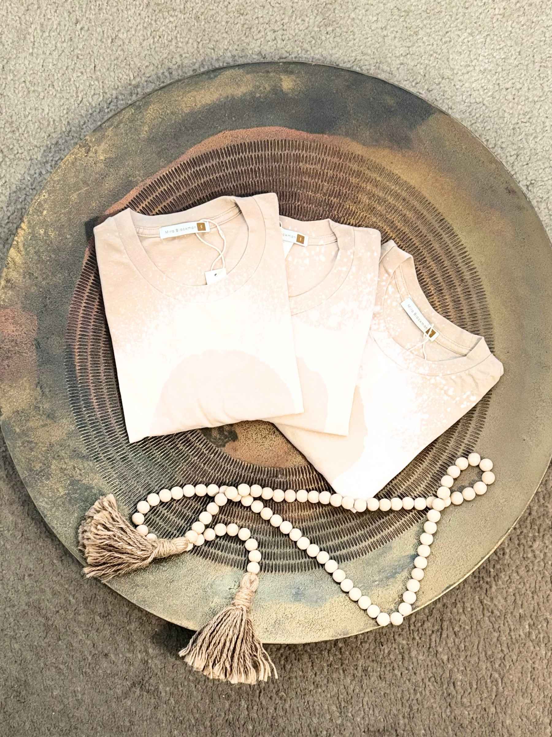 Flat lay of a group of Luminary Organic Tees by Mira Blackman in Neutral and styled with meditation beads.