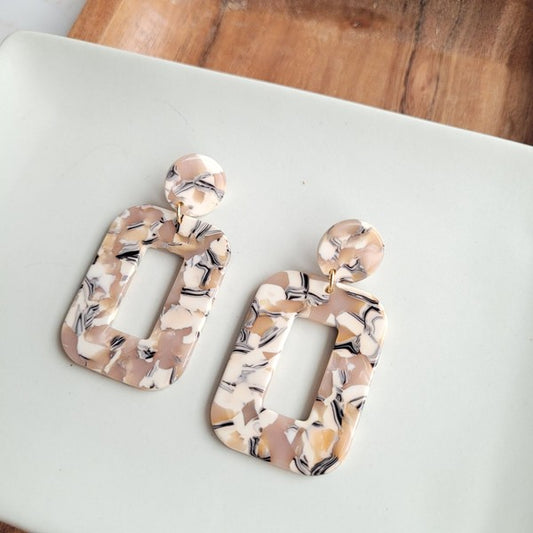 Tilted view of Handmade Sandstone Earrings on white table with wooden bowl in background.