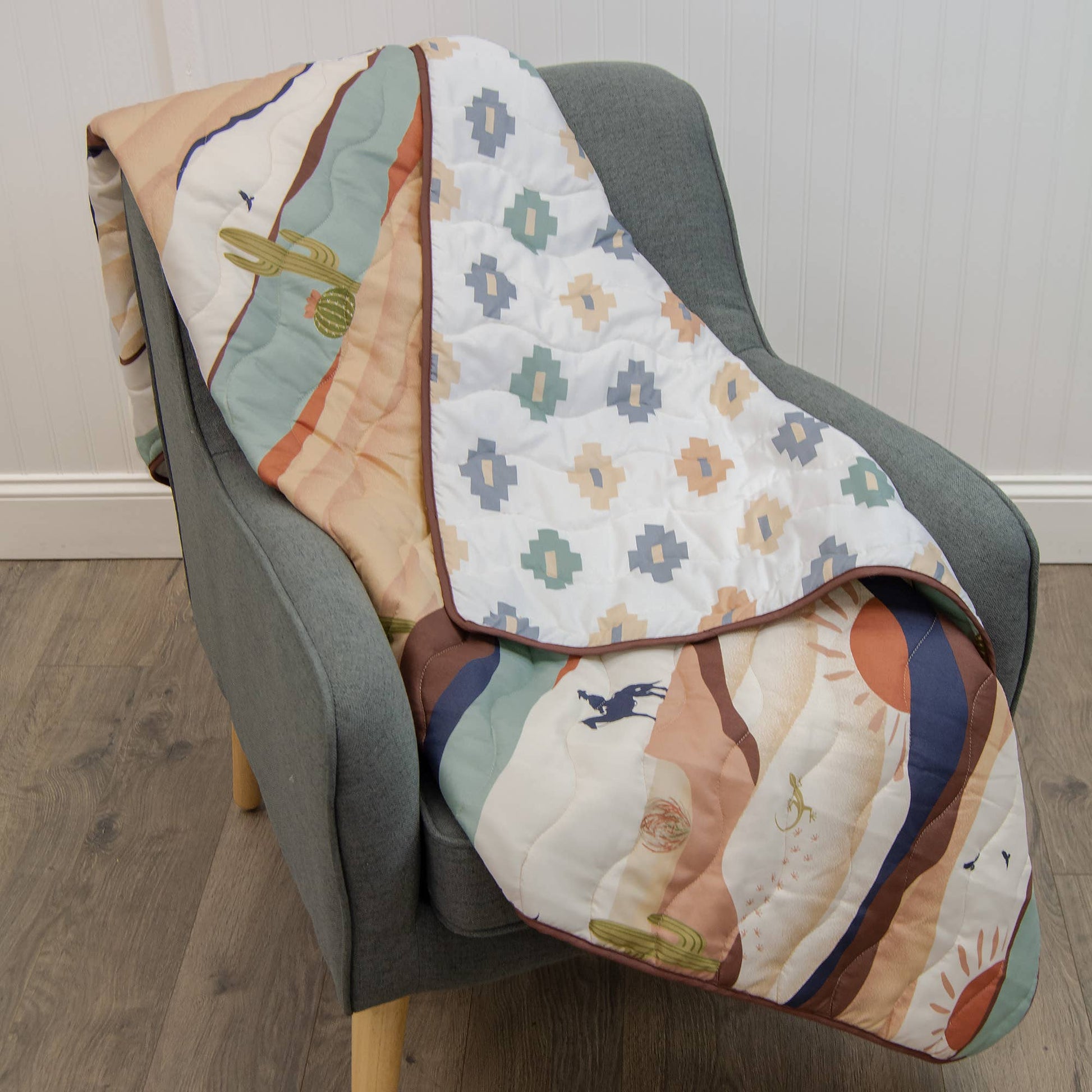 Earth-toned woven Journey throw with cowboy, cactus and sun design, draped over a neutral chair. 