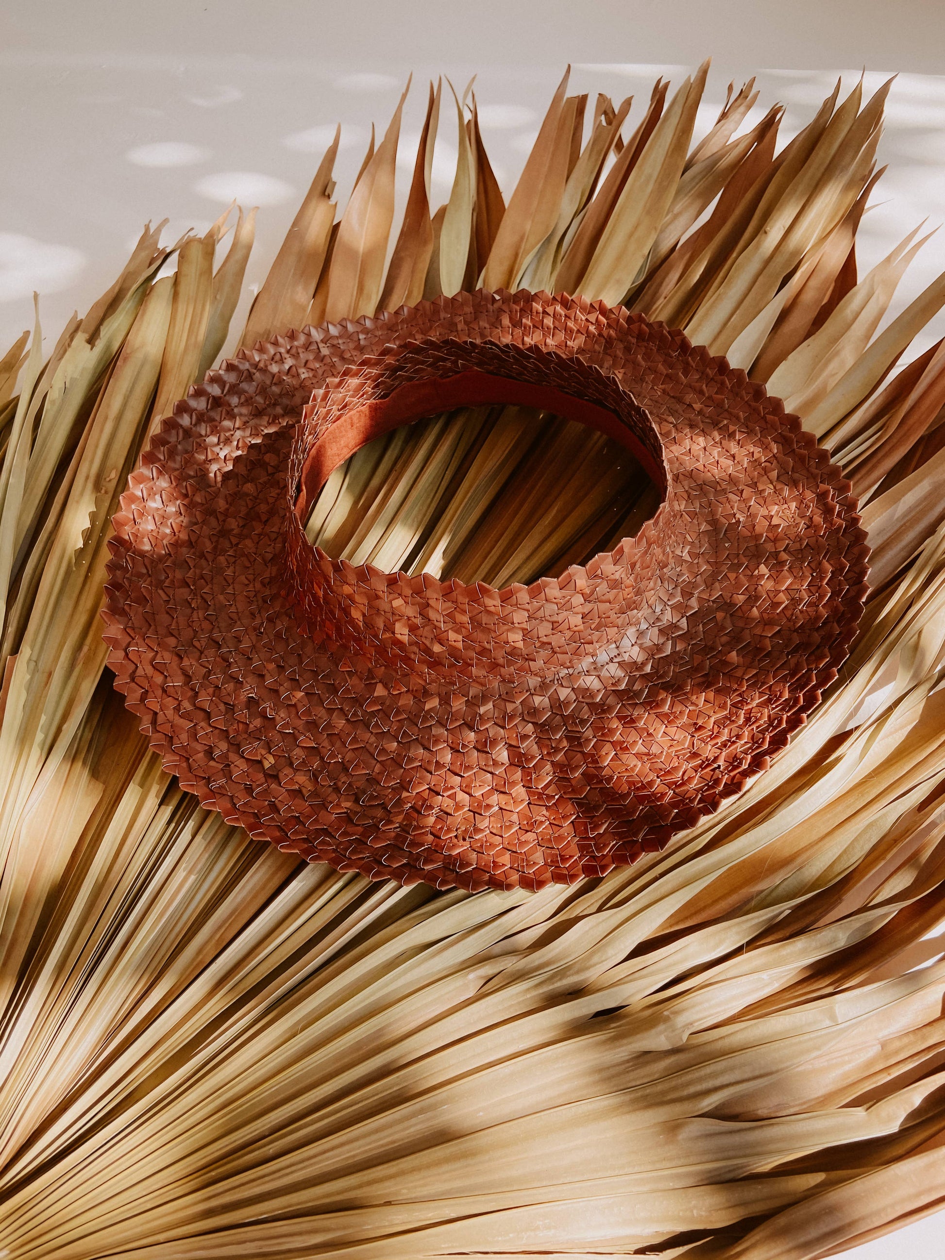 Papale Sun Hat in Clay resting on large leaves in sun.