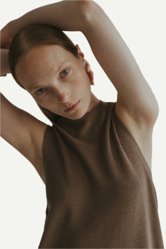 Model wears Taupe knit sweater vest with a mock neck and has arms in air. 