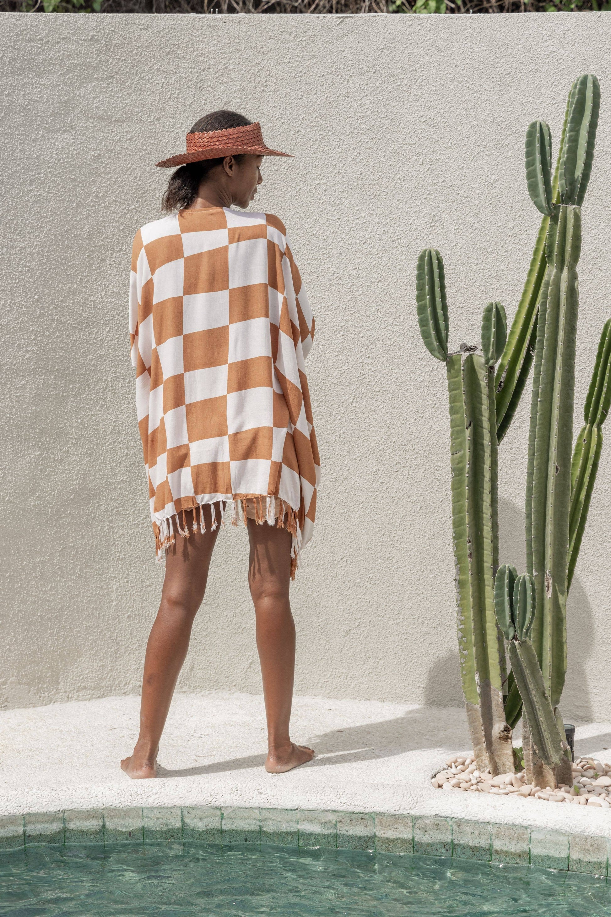 Back view of Papale Sun Hat in Clay. model stands by pool and cactus wearing hat and kimono. 