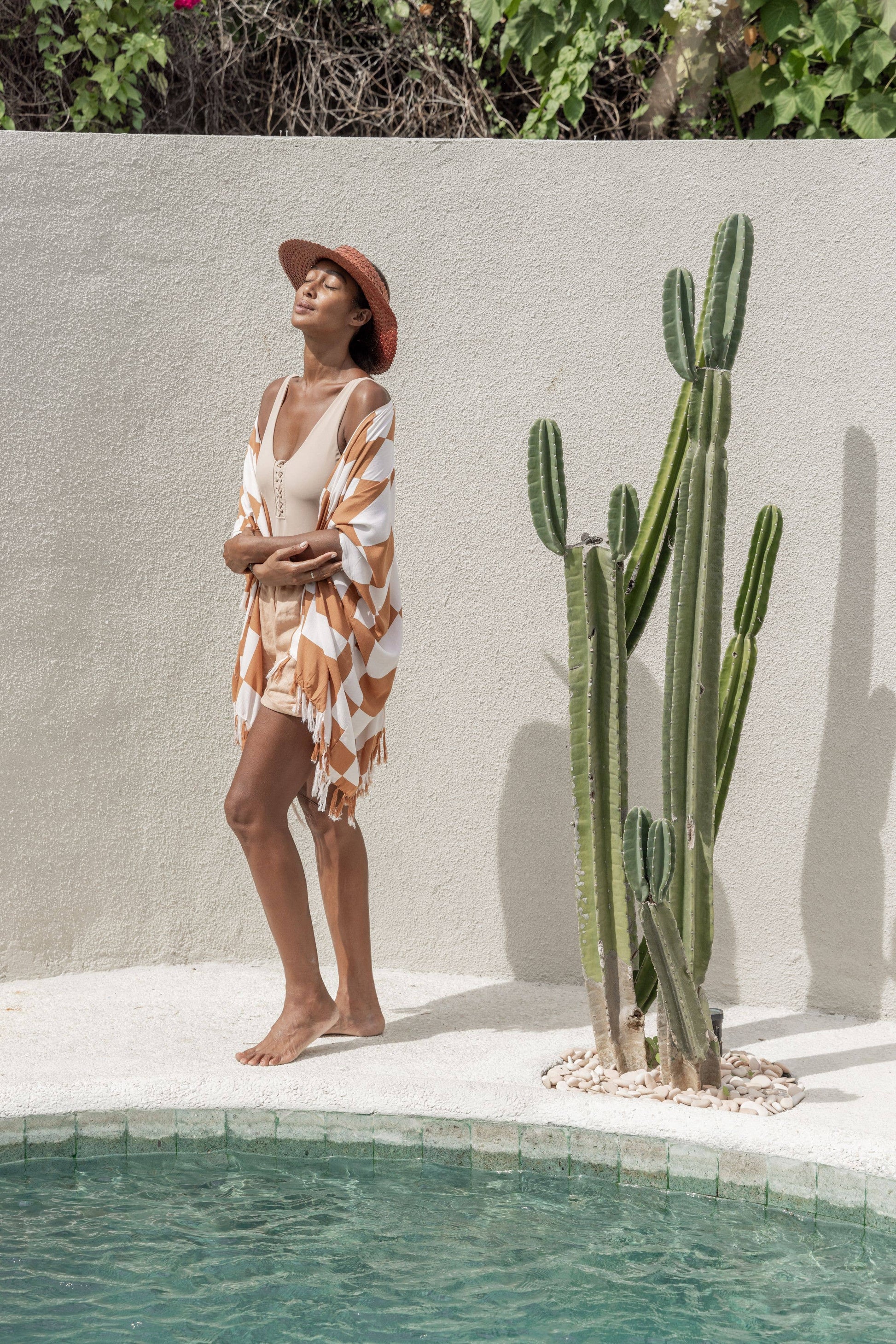 Lifestyle image of model wearing Papale Sun Hat in Clay standing by the pool and wearing a kimono. 