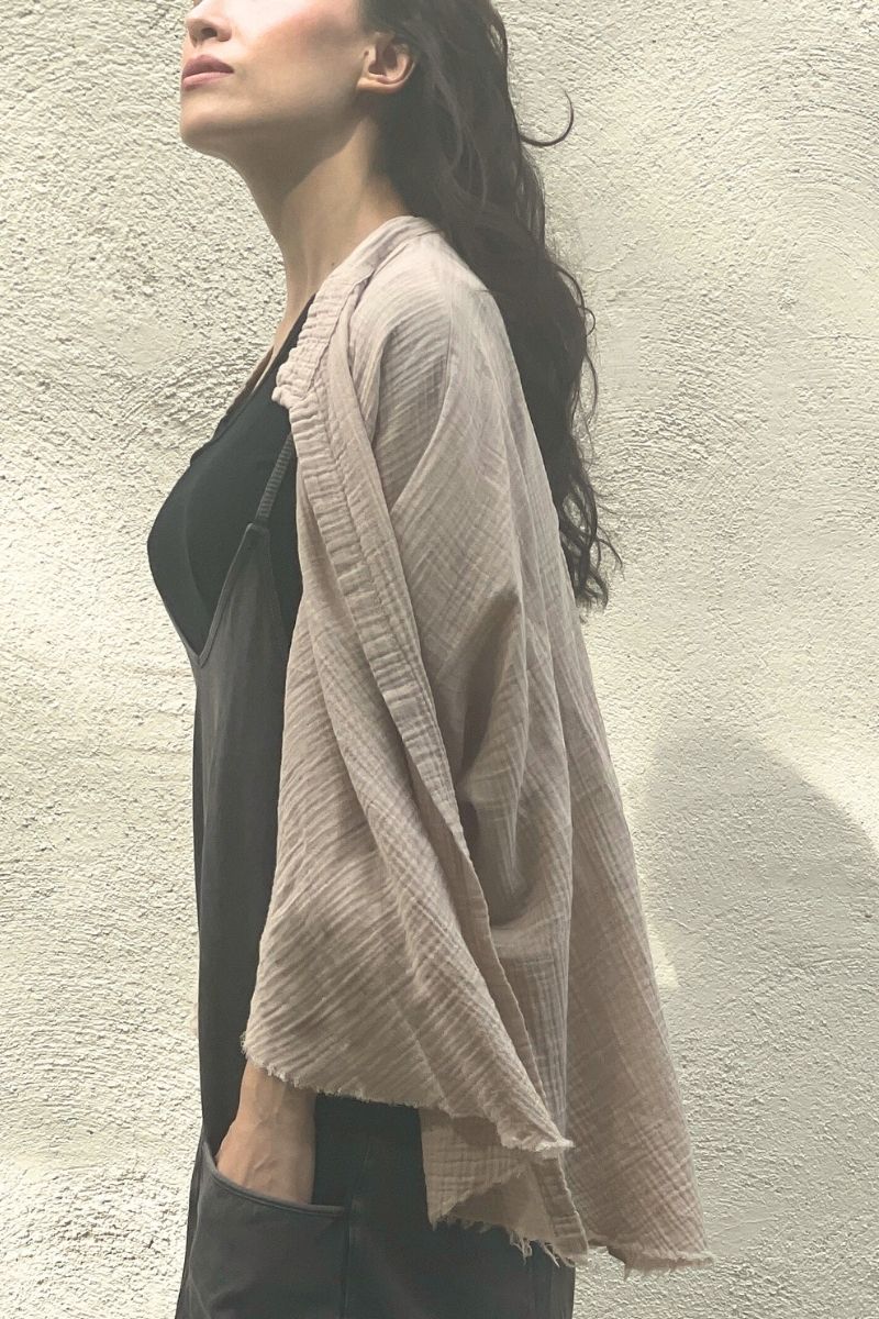 Model wearing a beige muslin kimono over a black top and jumpsuit against a light-colored wall.