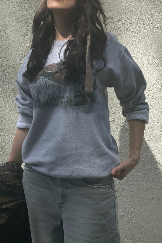 Person wearing a gray sweatshirt with a vintage duck graphic design against a plain wall.