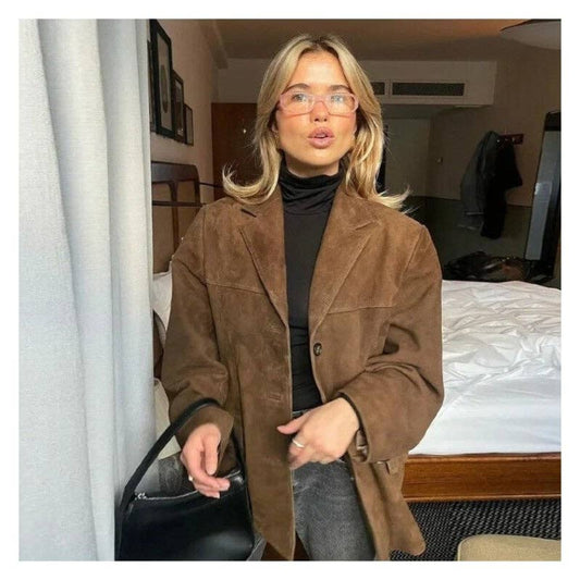 Brown cropped suede jacket with a minimal silhouette and vintage-inspired look. Model wears with glasses and black leather bag. 